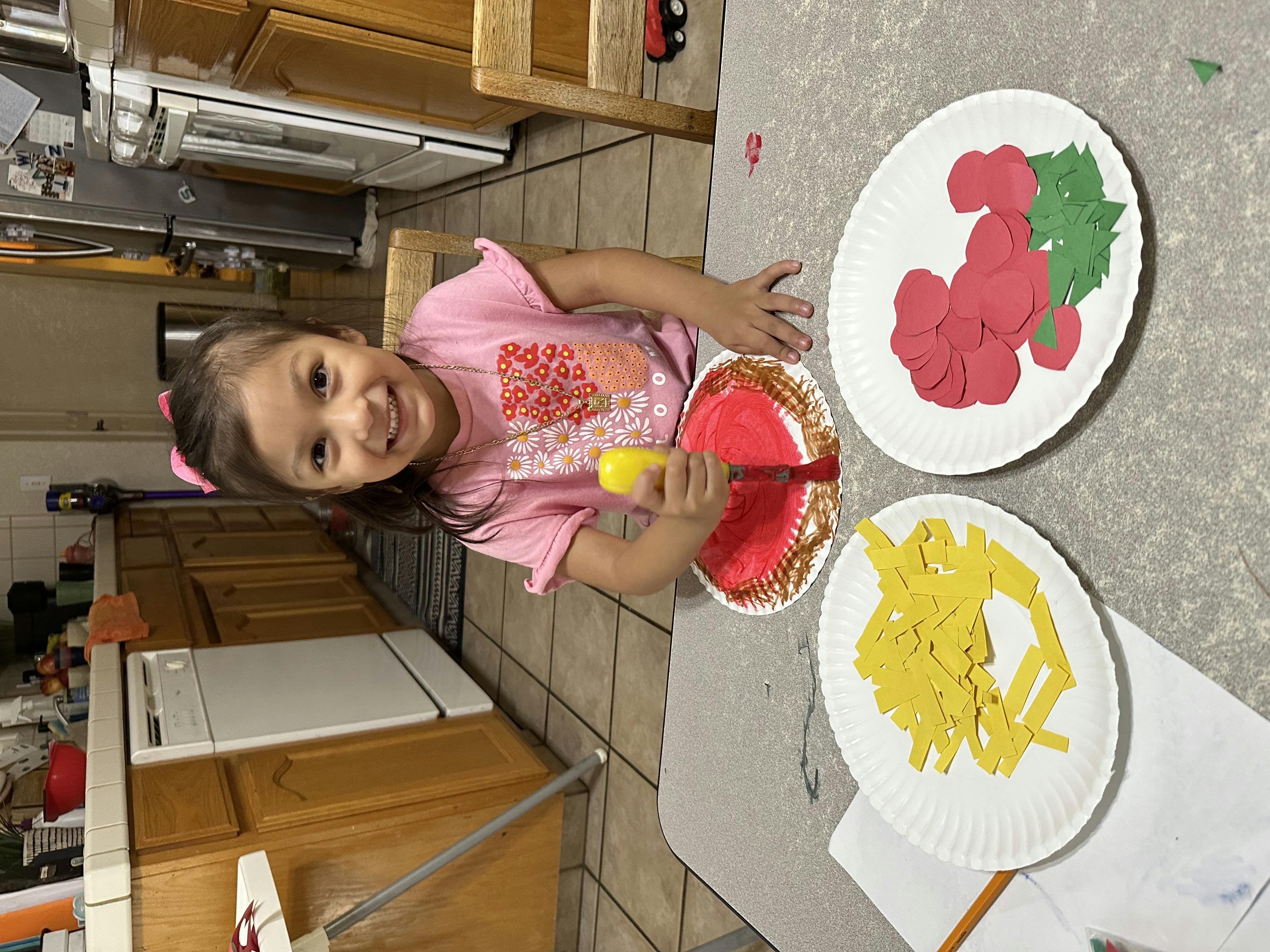 Child making paper plate crafts with red and green paper cutouts
