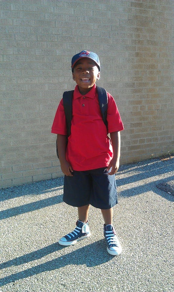 Child wearing a red shirt, shorts, and backpack standing with a backpack