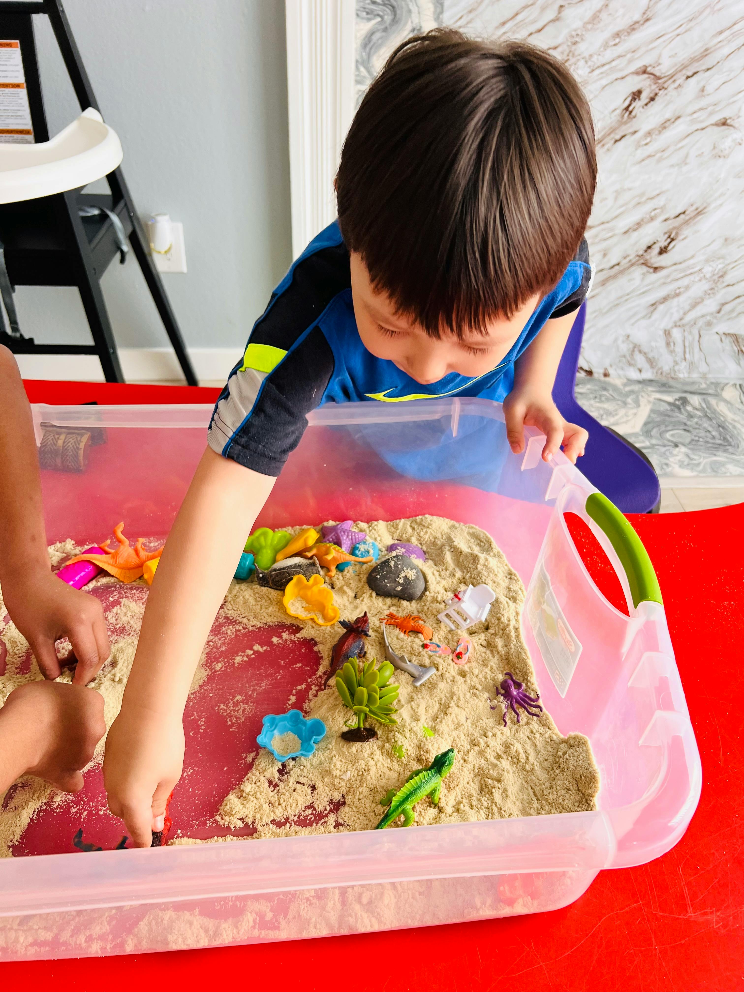 Child playing with sand and toys in a clear bin
