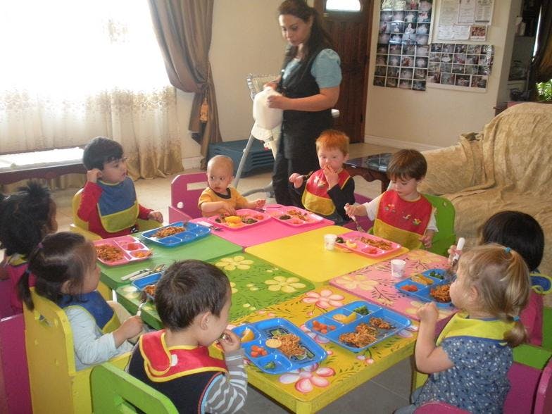 Adult standing near a table with multiple children eating