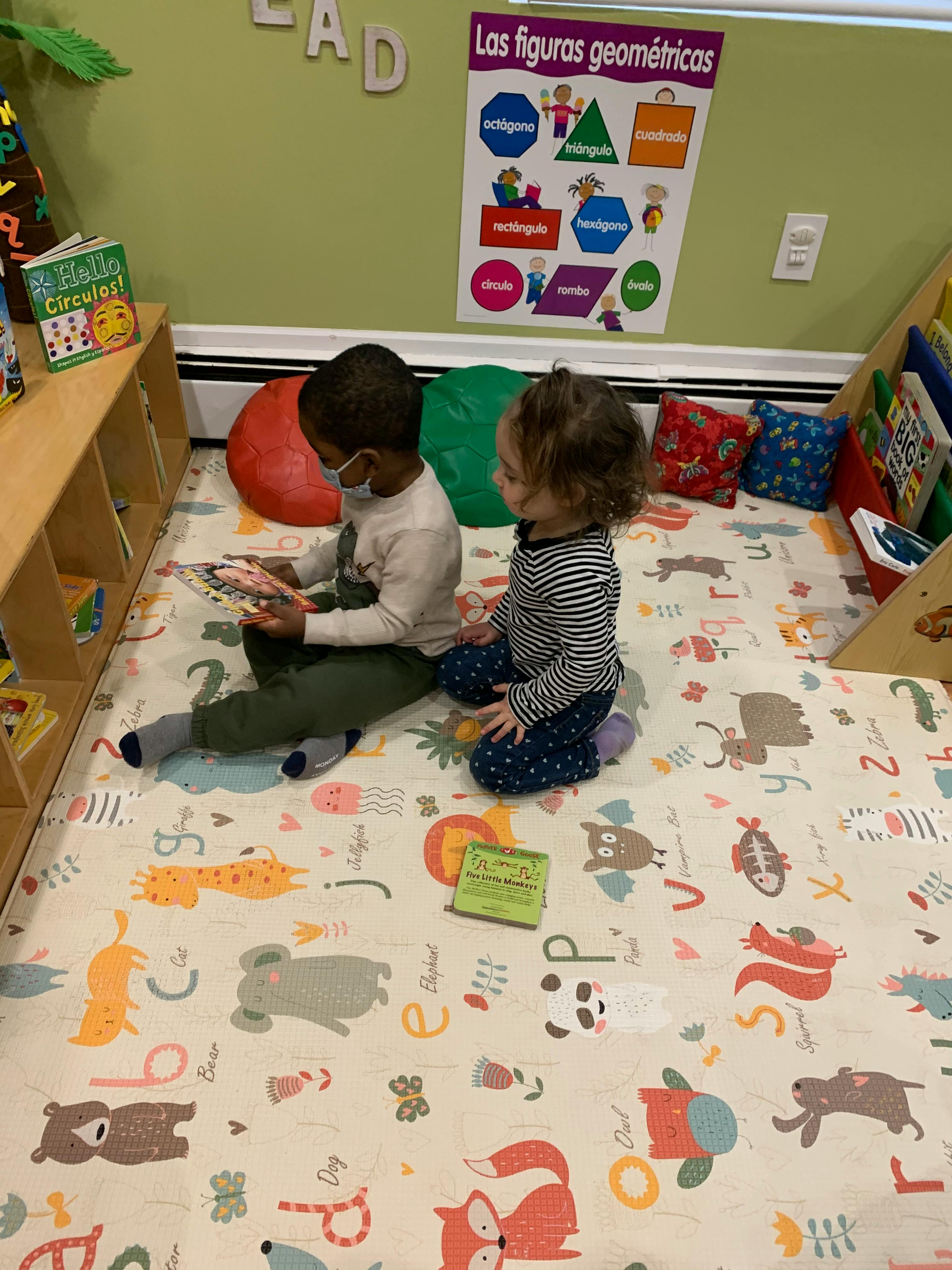 Two children sitting on a mat, one reading a book