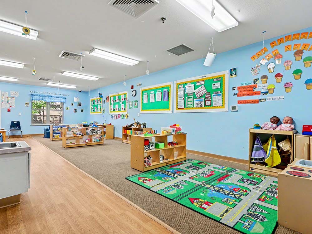 An empty early childhood classroom with toys, bulletin boards, and a play rug