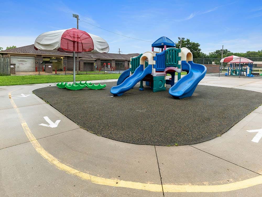 Playground with blue and green playset, slides, and red and white umbrella