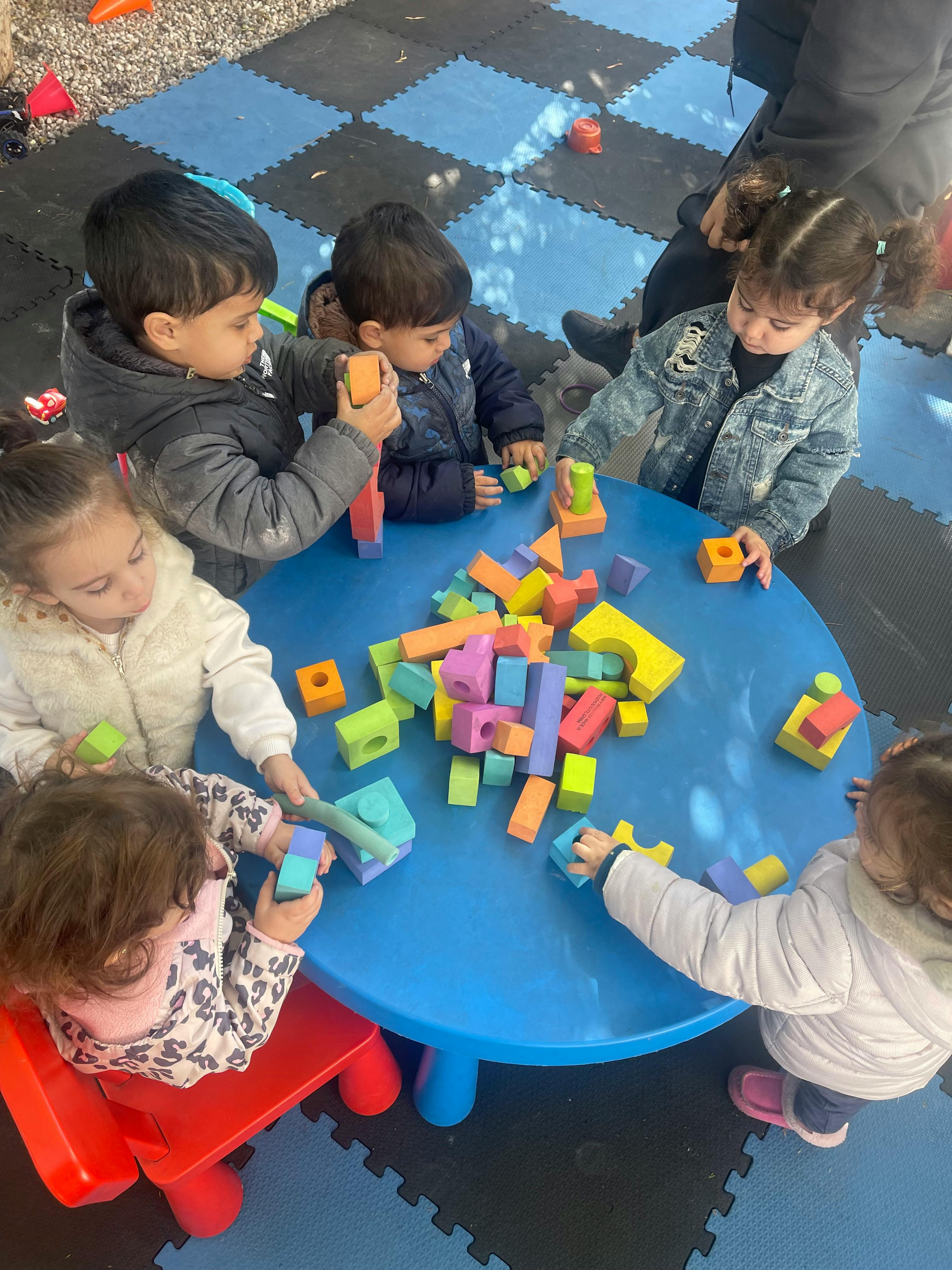 Children playing with colorful building blocks at a blue table