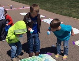 Three children painting on paper outdoors