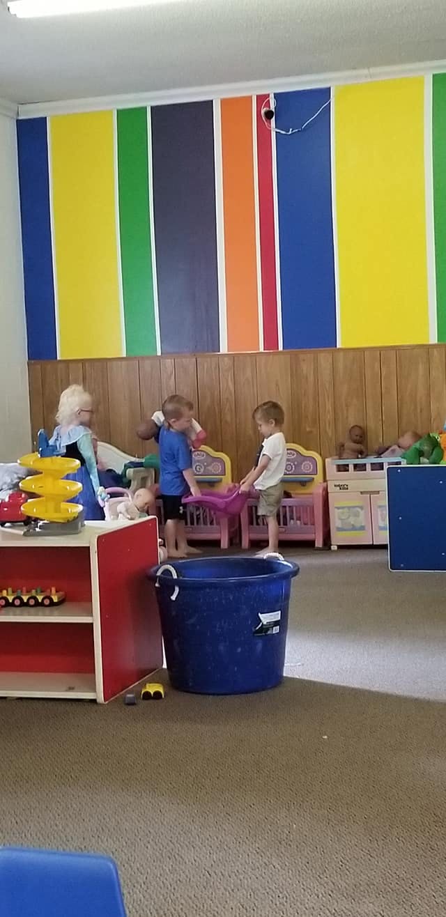 Three children playing with toys in a room with a colorful striped wall