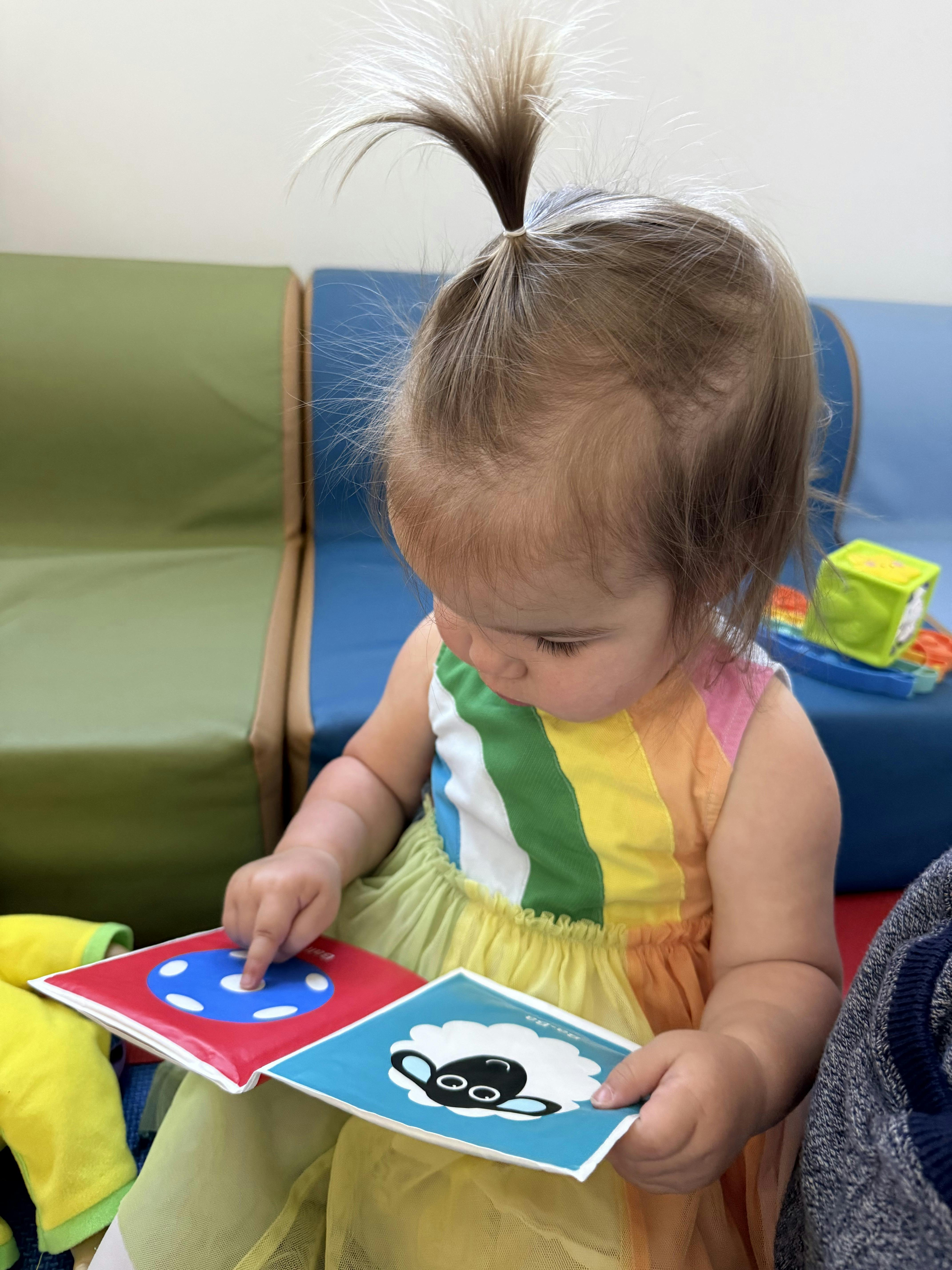 Child in a rainbow dress reading a book while pointing at a page