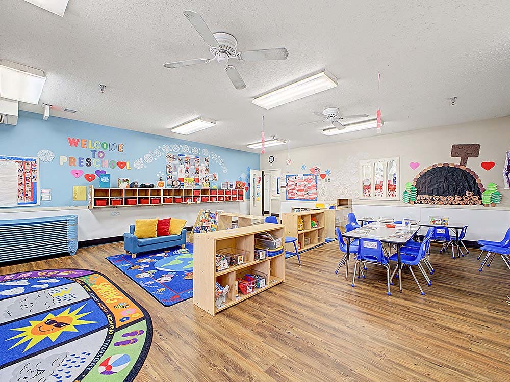 An empty preschool classroom with colorful decorations, small tables and chairs