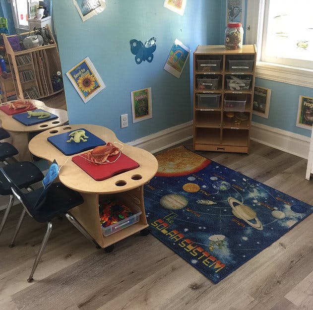 Classroom with small tables, chairs, and a solar system rug