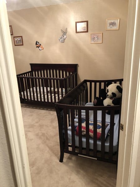 Two dark wooden cribs in a room, one with a panda stuffed animal