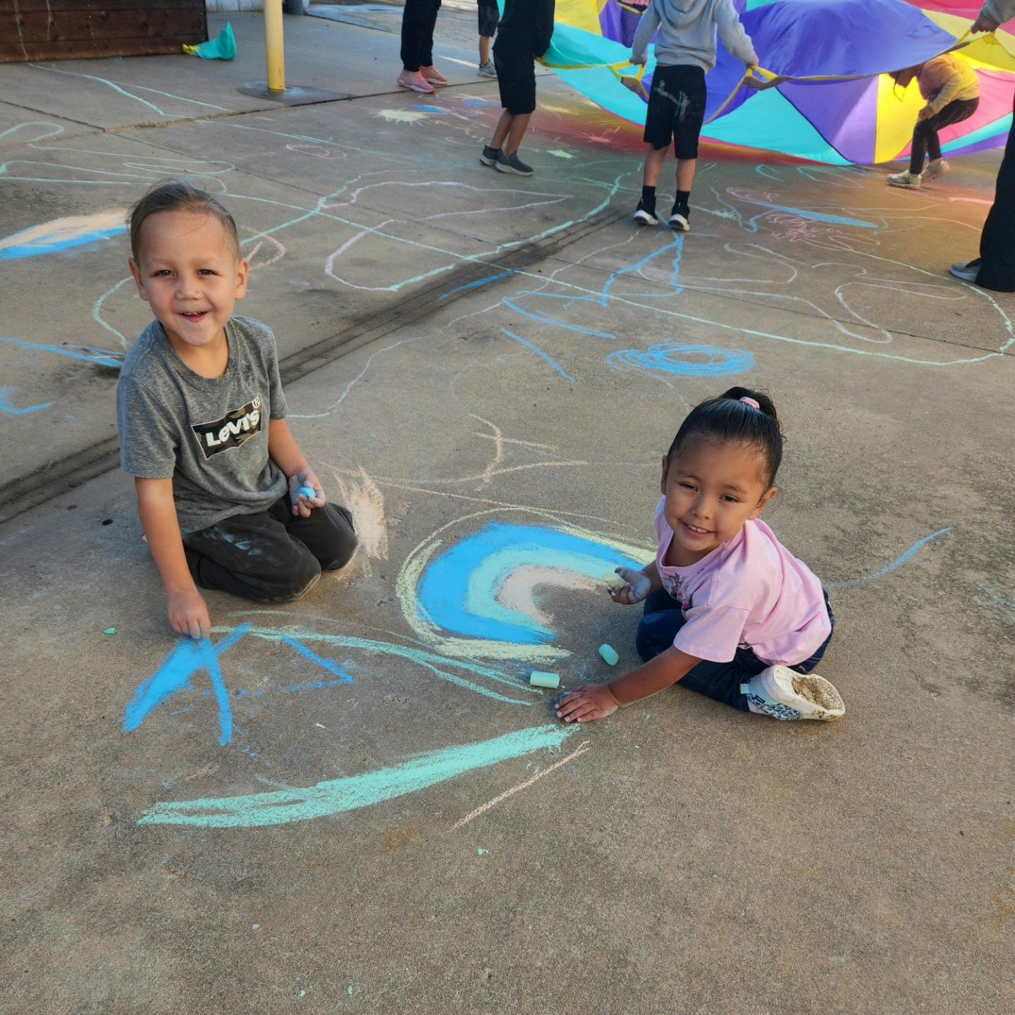 Two children drawing with chalk on pavement