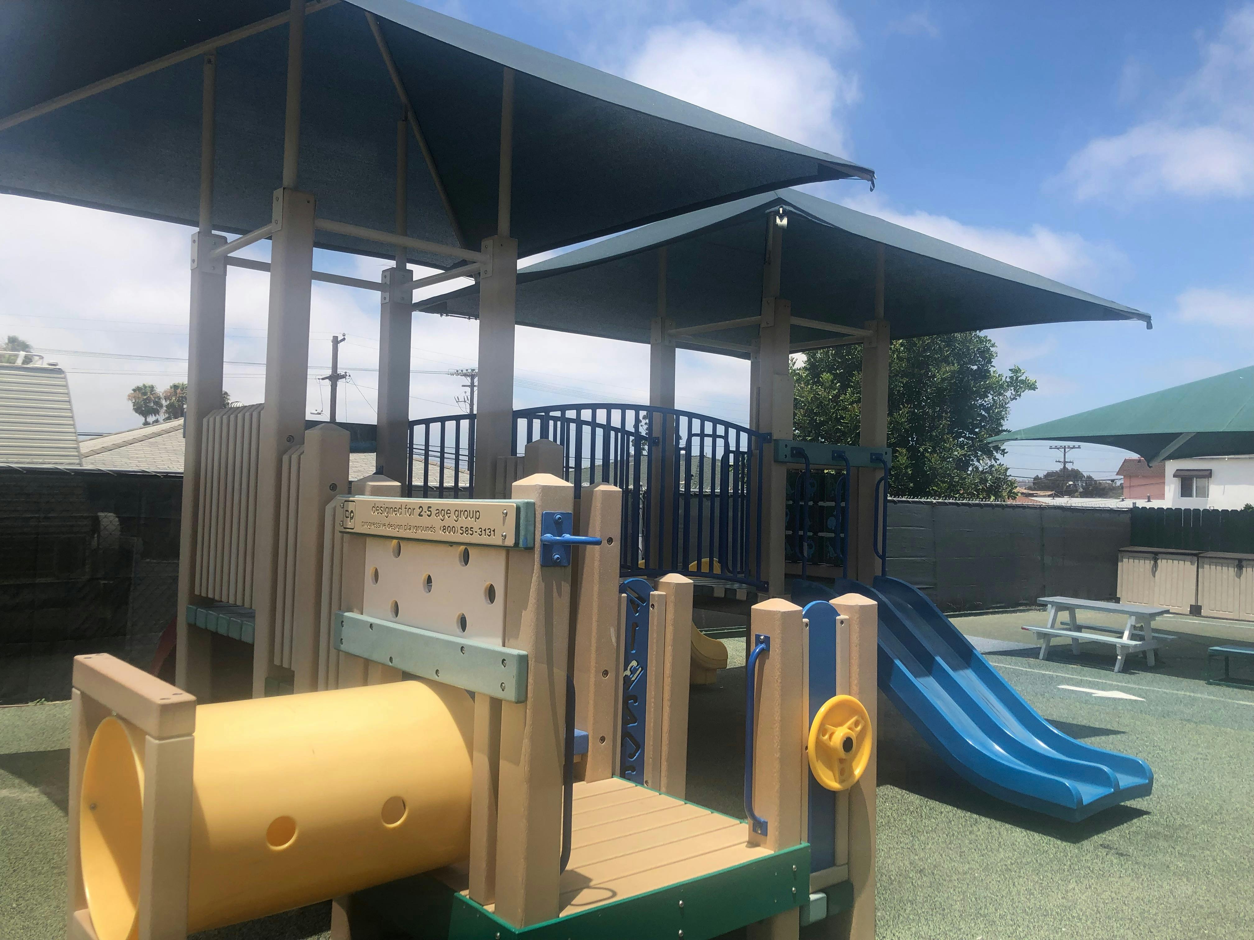 Playground with a yellow tunnel, blue slide, and shaded structures