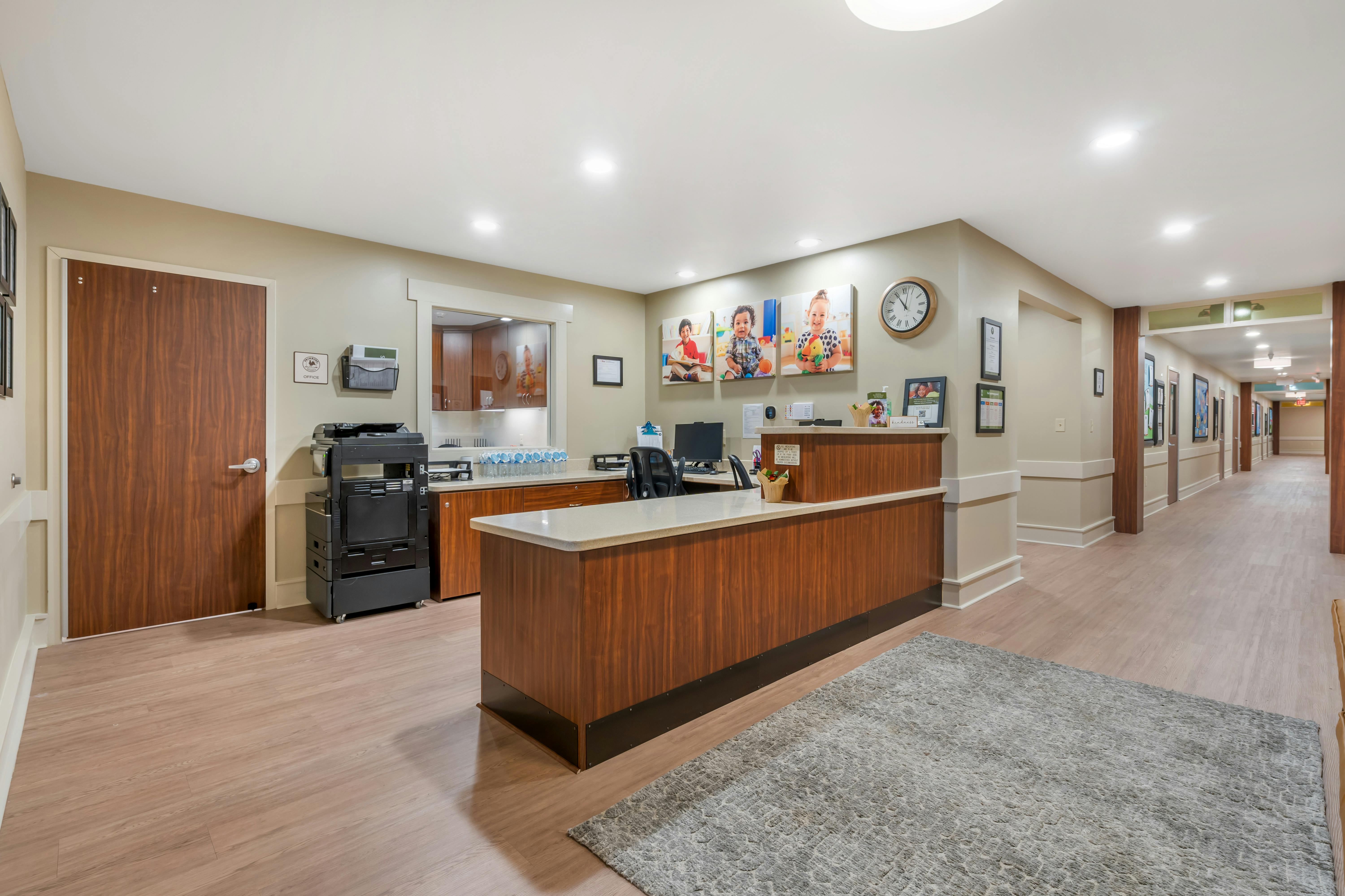 Reception area with a wooden desk, computer, and child portraits on the wall