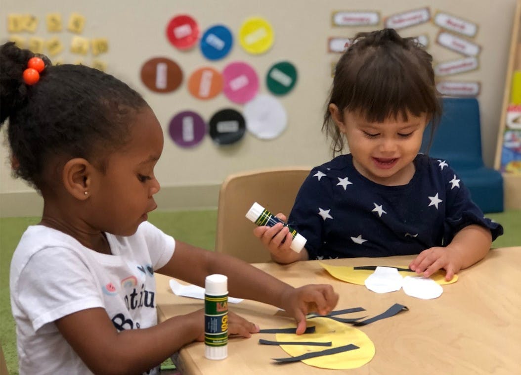 Two children doing crafts at a table in a classroom