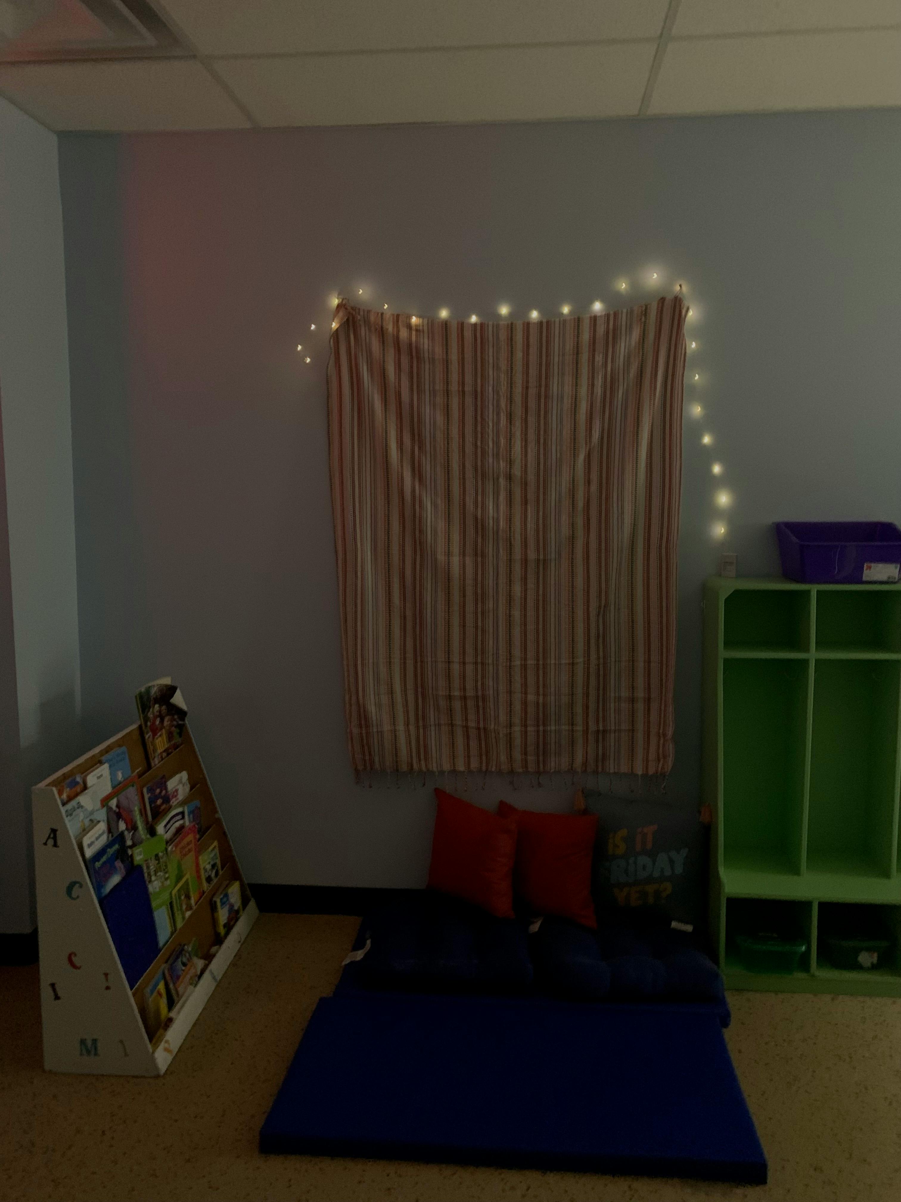 Reading nook with a striped curtain, string lights, floor cushions, and a book display