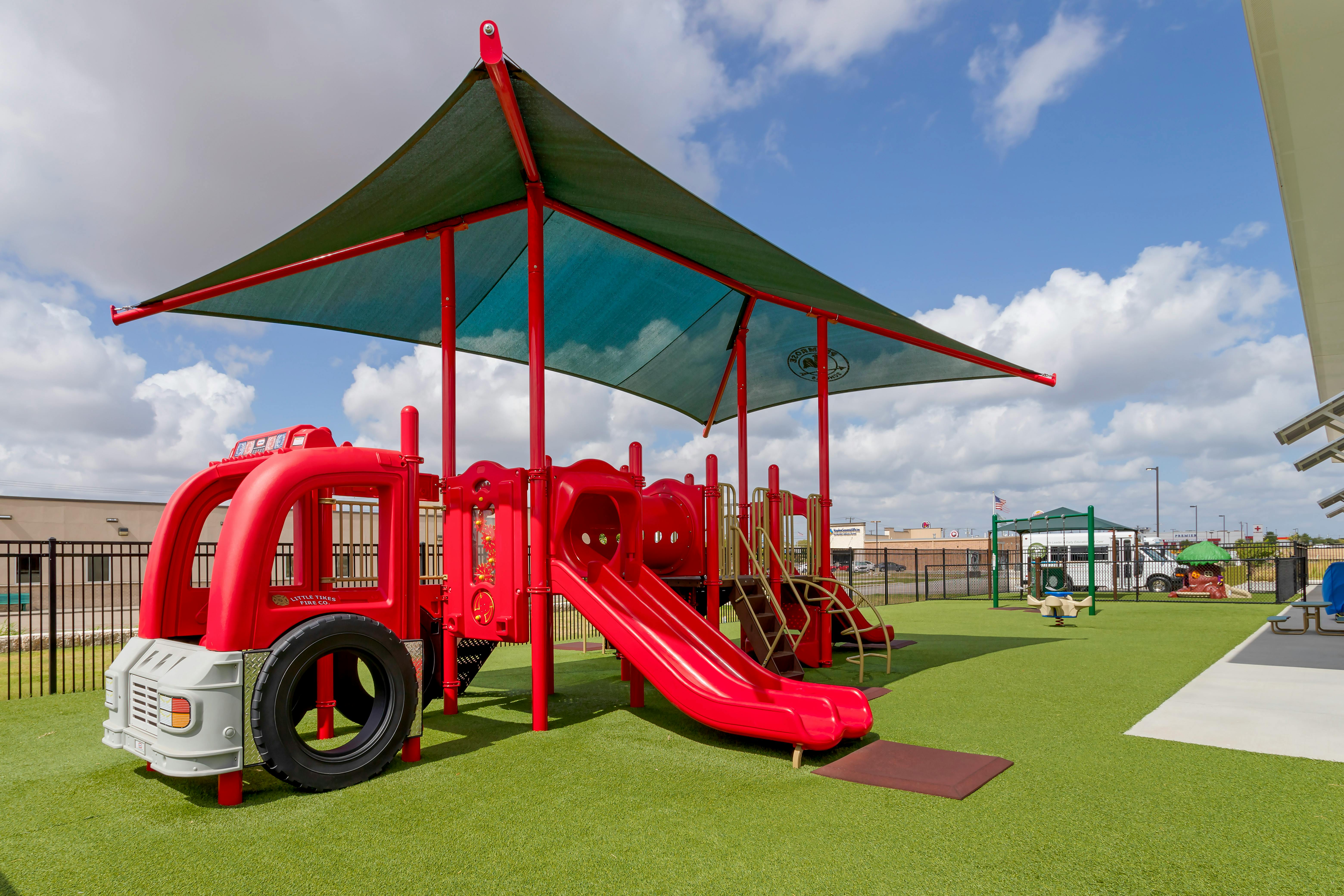 Red fire truck-shaped playground structure with slides on artificial turf
