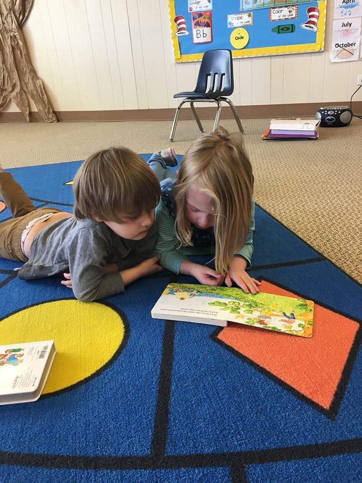 Two children lying on a rug reading a book together