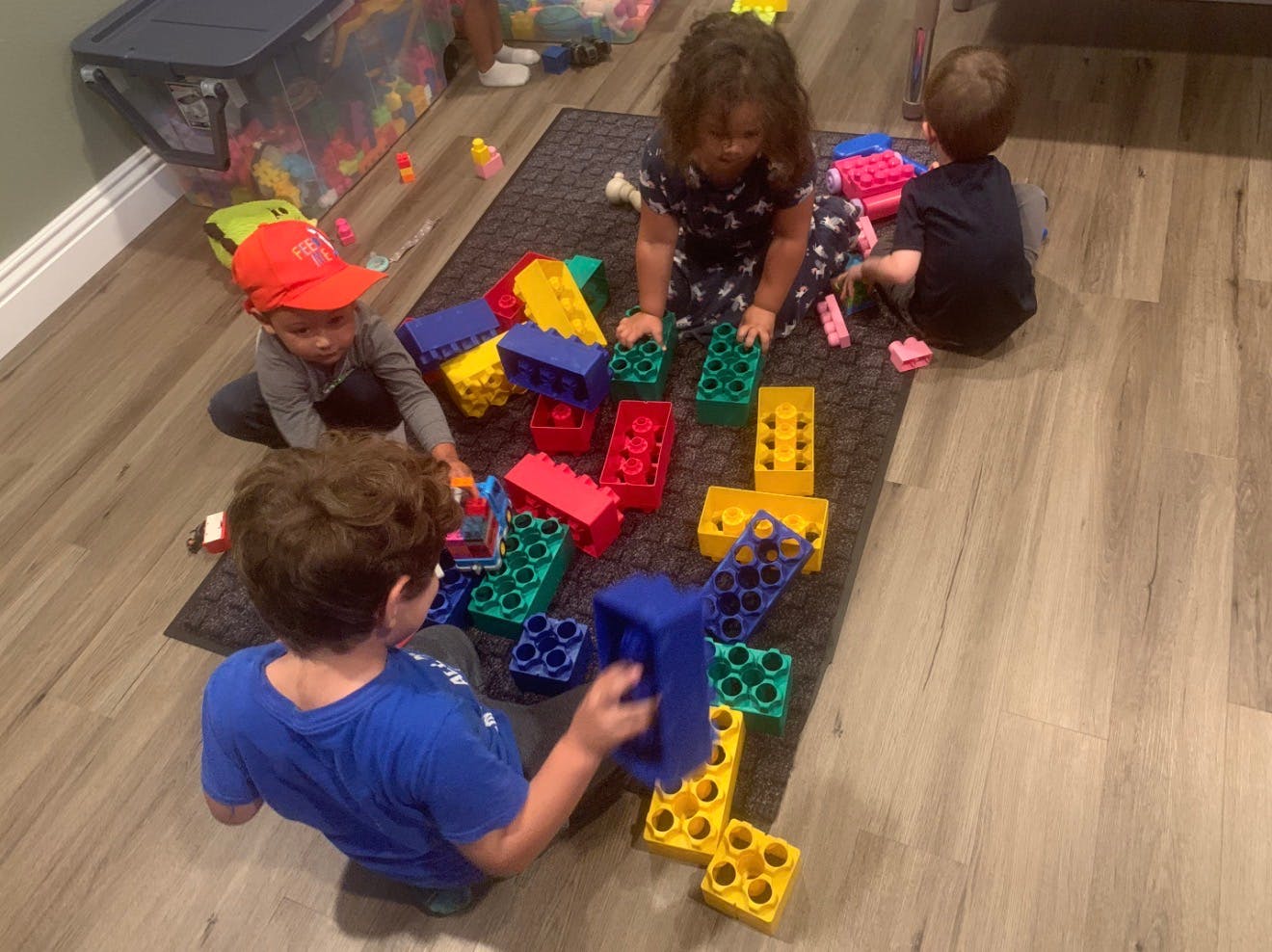 Three children playing with colorful building blocks on a rug