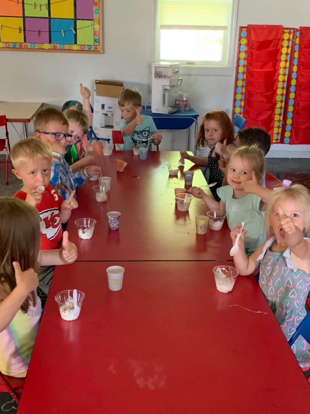 Children sitting at a red table with cups