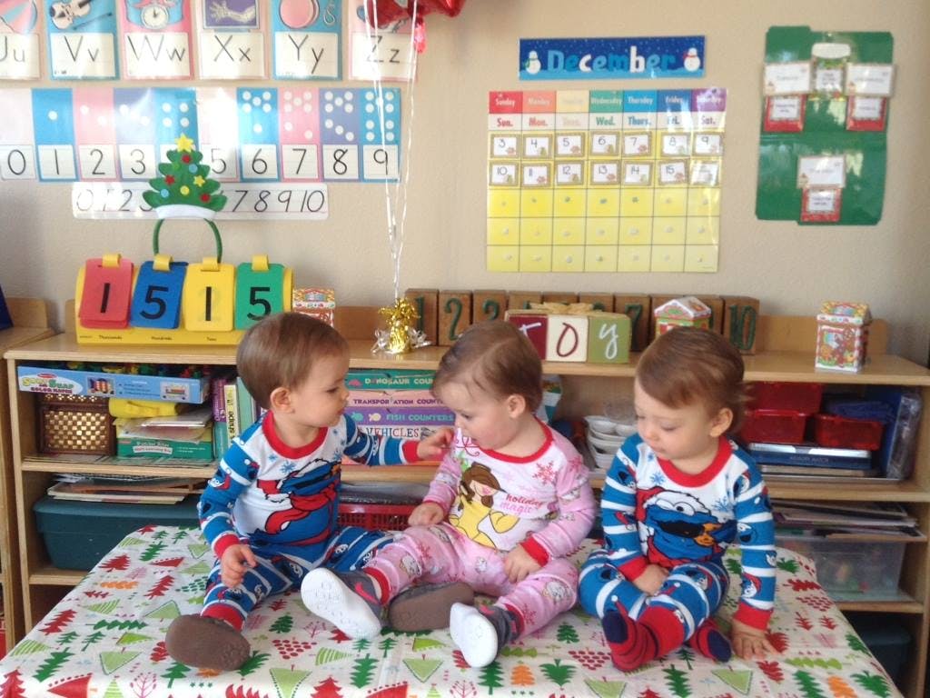 Three children in pajamas sitting on a patterned blanket in a classroom
