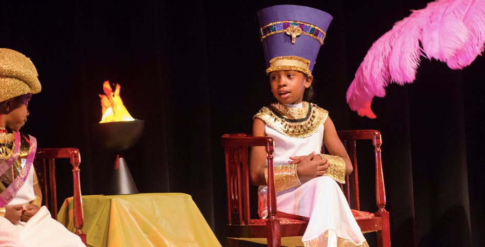 Child in costume with a tall purple hat sitting on a chair