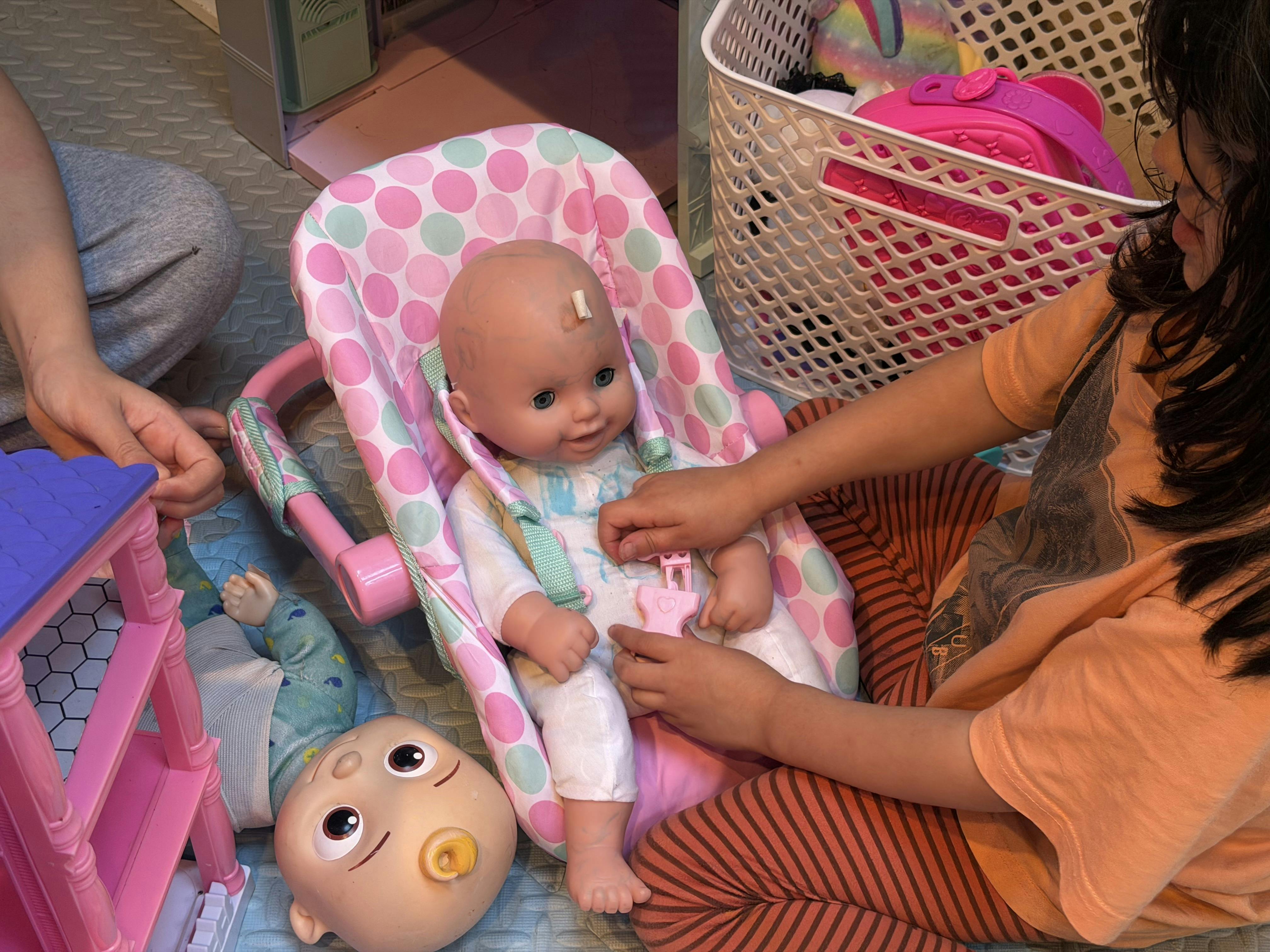 Child playing with a baby doll in a small pink carrier