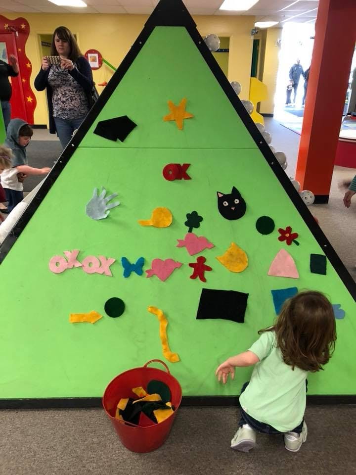 Child playing with felt shapes on a green pyramid-shaped board