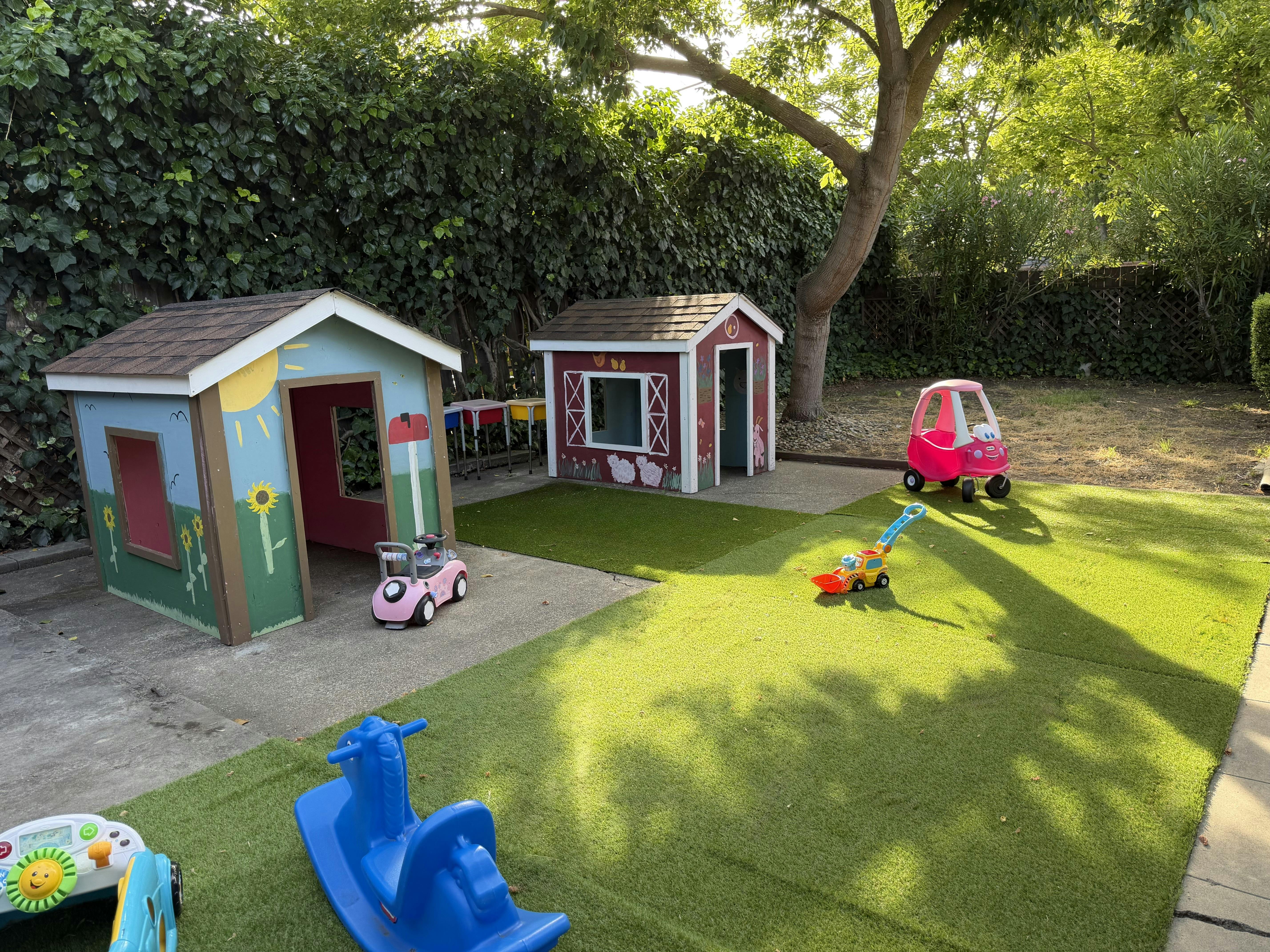 Playhouses and ride-on toys in a yard with artificial turf