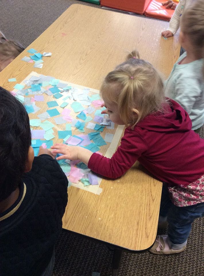 Two children doing a craft with colorful paper squares on a table