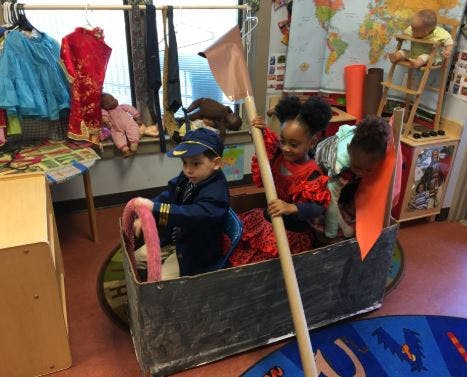 Three children playing in a cardboard boat in a classroom