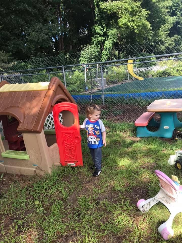 Child standing next to a playhouse with a red door