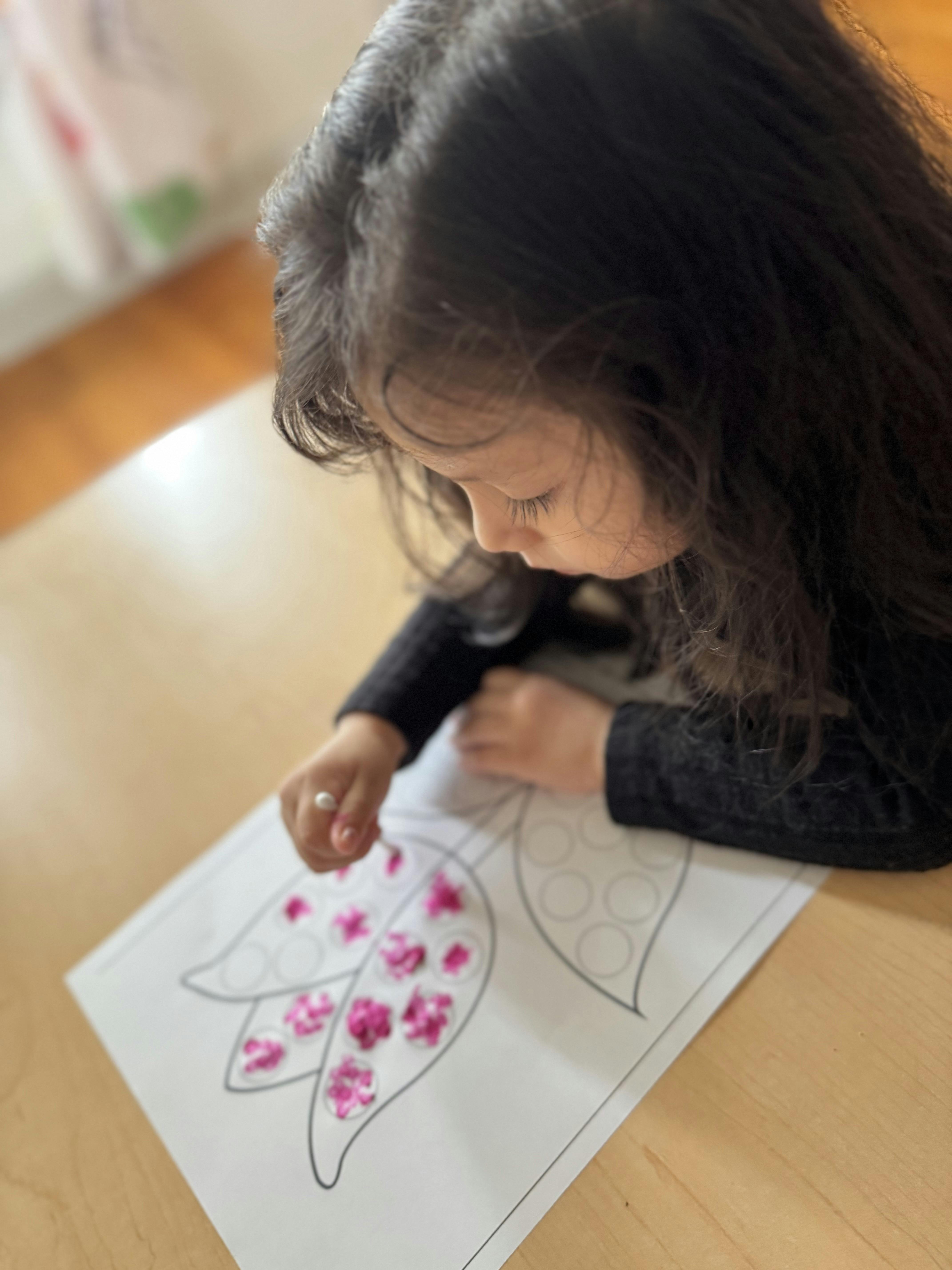 Child decorating a paper flower with small pink pieces