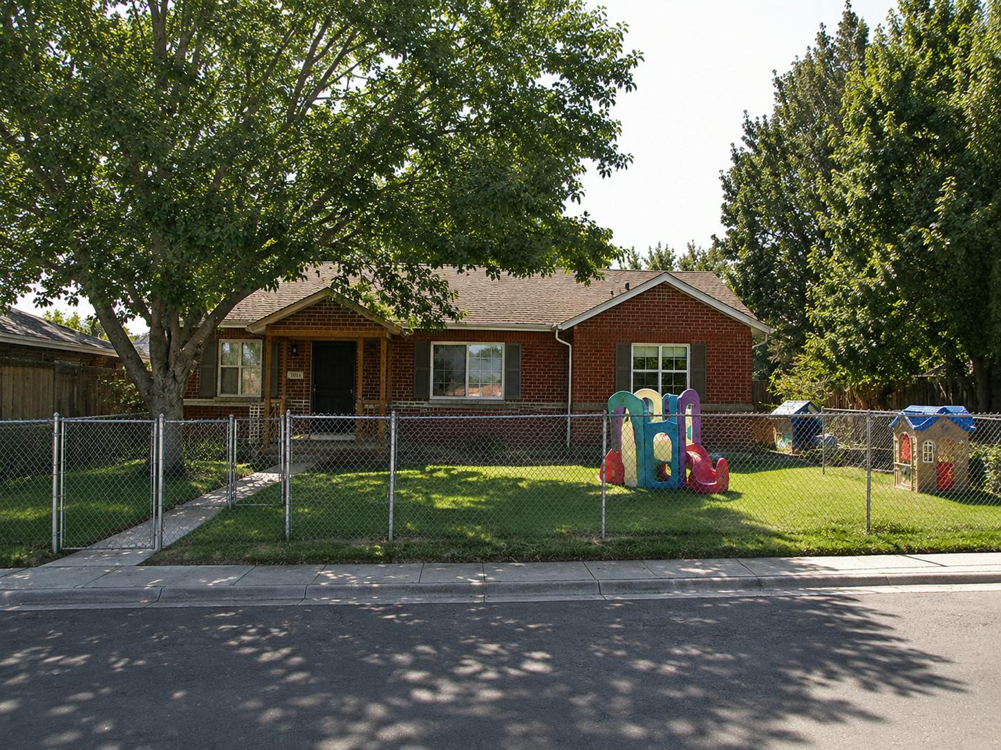 Single-story brick house with a fenced front yard and children's play equipment