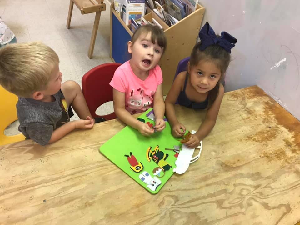 Three children playing with toys on a green mat at a table