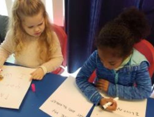 Two children writing on paper at a table