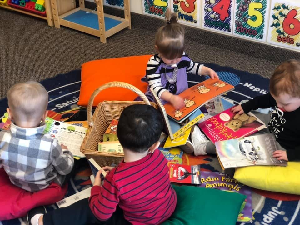 Three children sitting on a rug looking at books