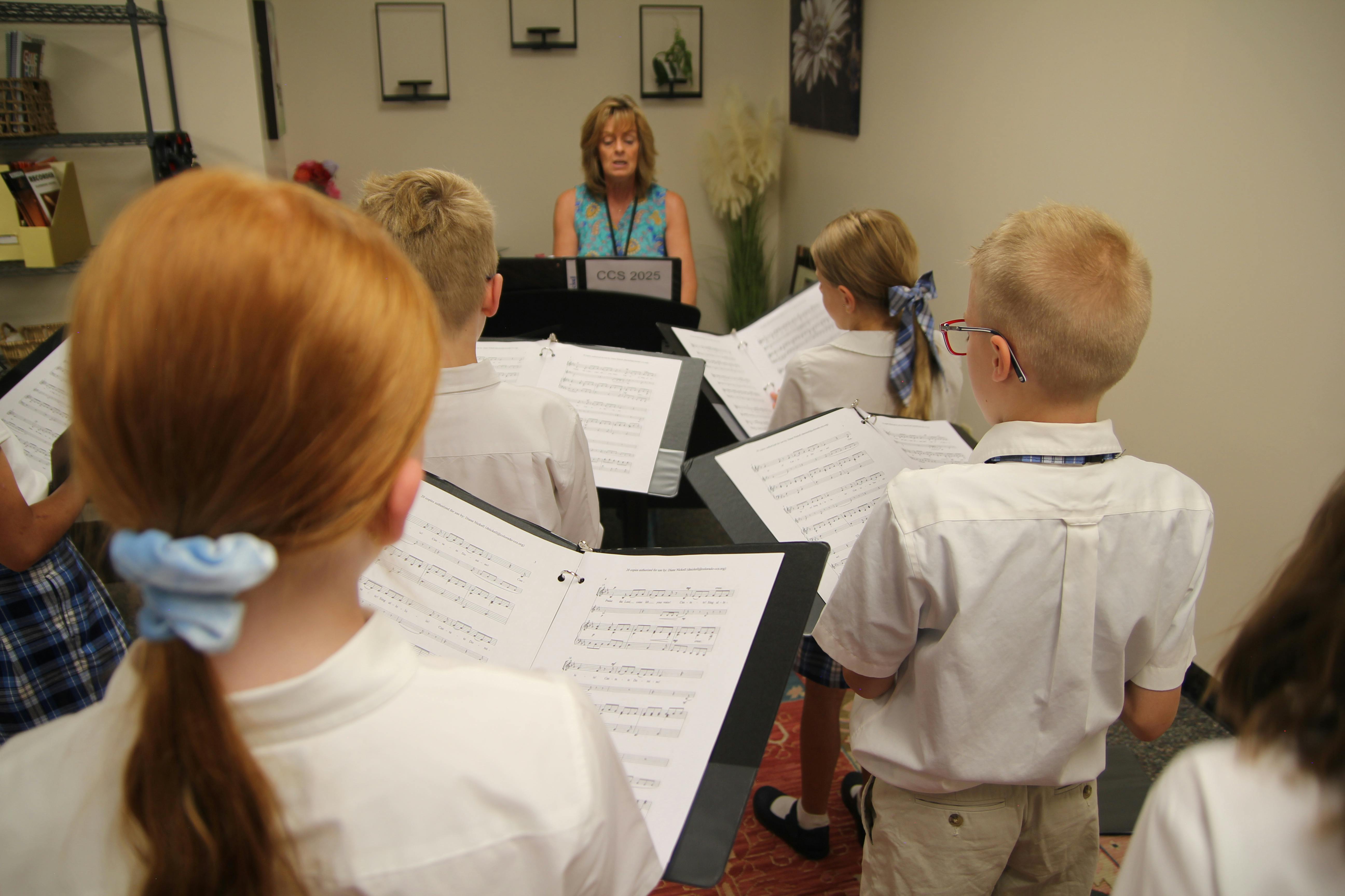 Adult leading a group of children reading music from stands