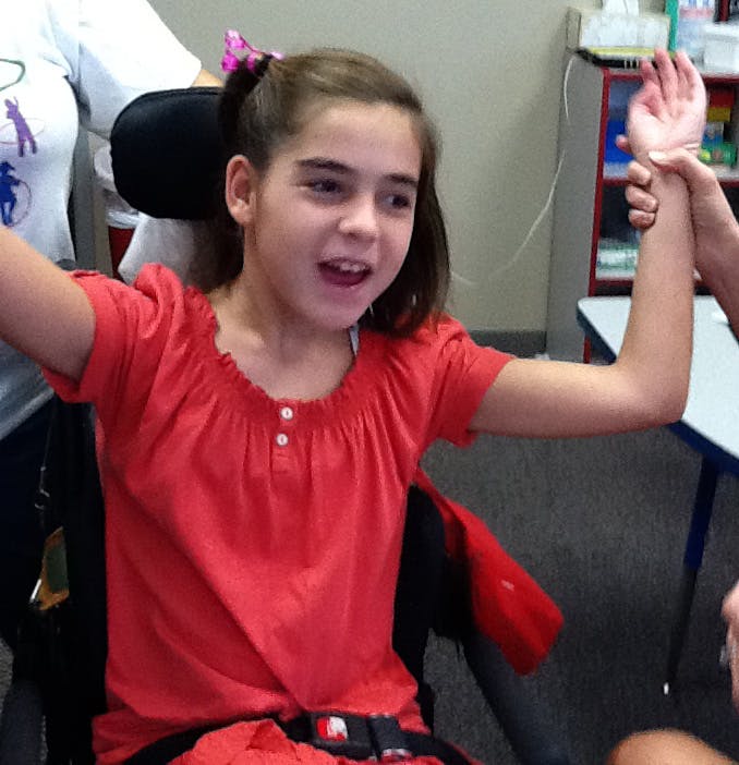 Child in a wheelchair with arms raised, one arm held by another person