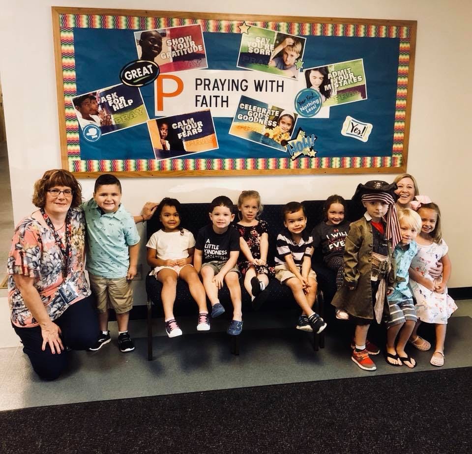 Adult and multiple children sitting and standing in front of a bulletin board