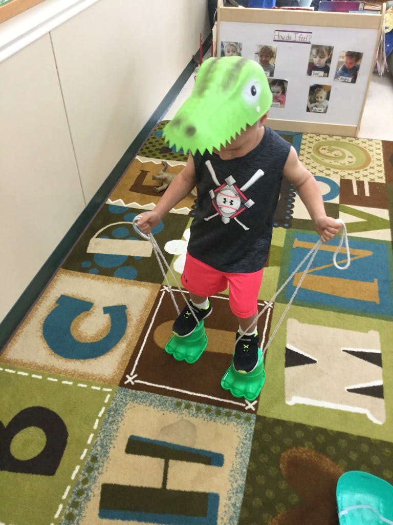 Child wearing a dinosaur mask and dinosaur feet walking on a rug