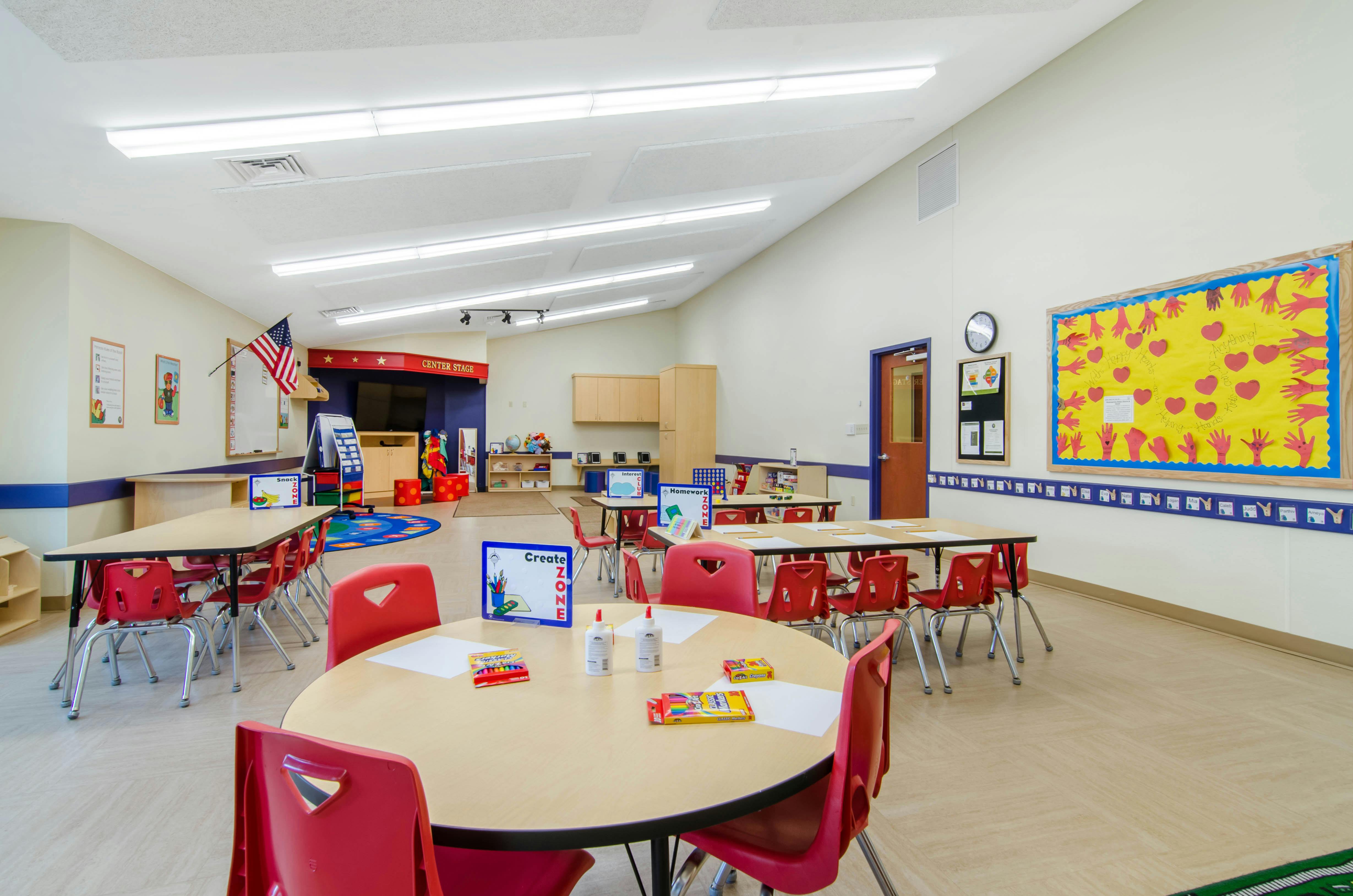 An empty classroom with multiple tables, red chairs, and various learning aids