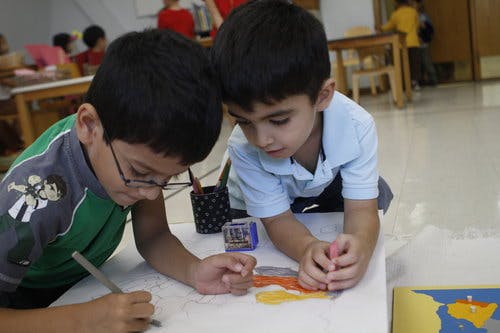 Two children drawing and working on a puzzle in a classroom