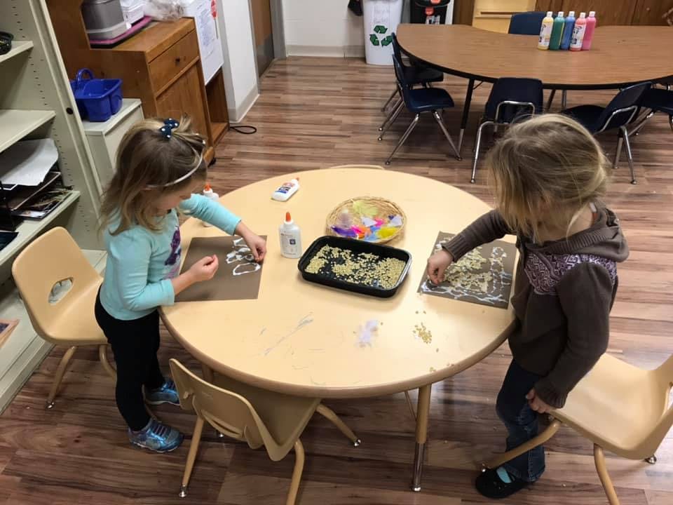 Two children doing crafts at a table in a classroom