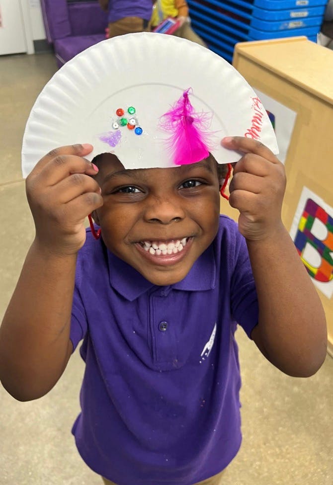 Child holding up a paper plate craft with feathers and beads