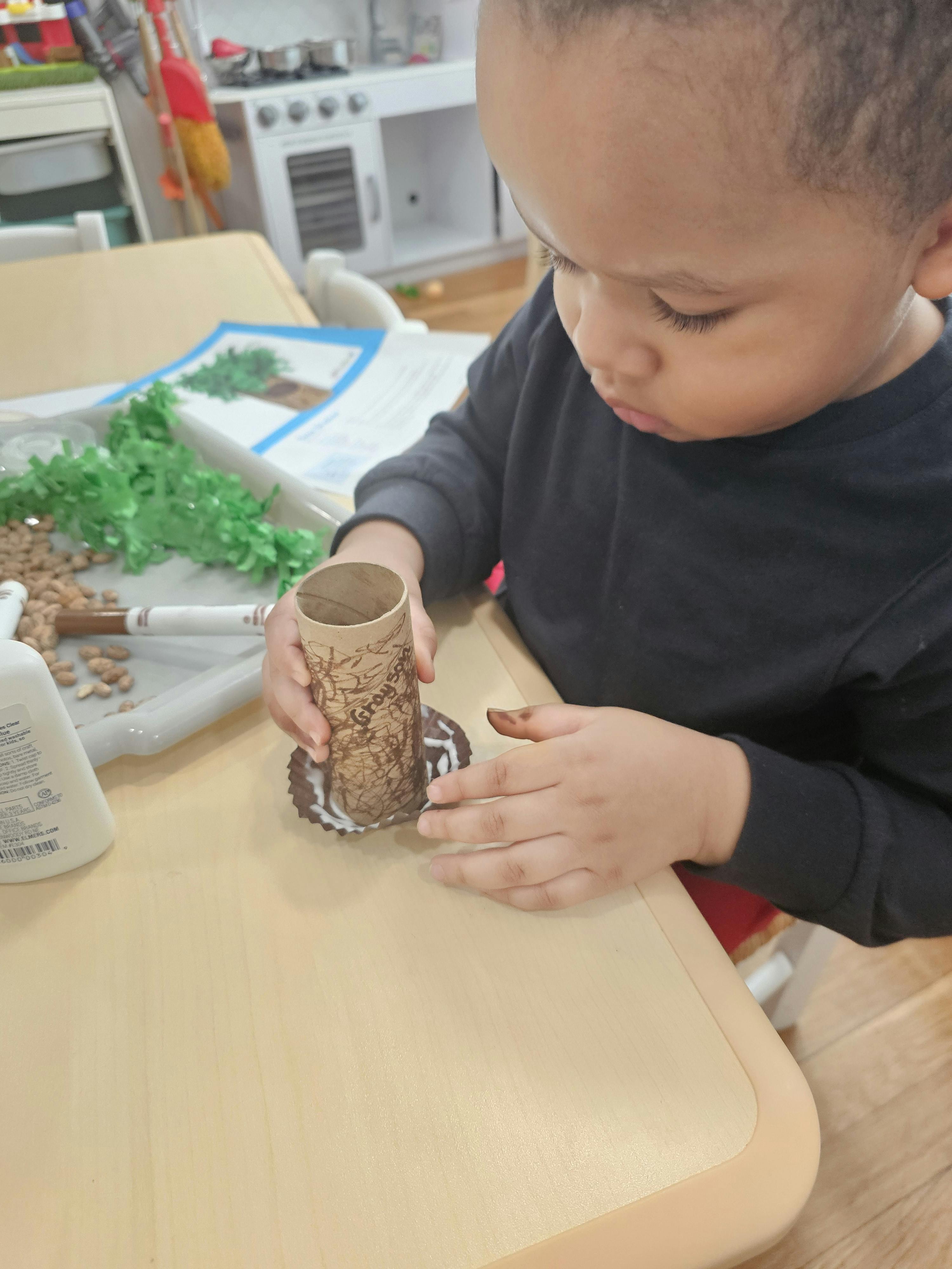 Child decorating a cardboard tube with a textured pattern