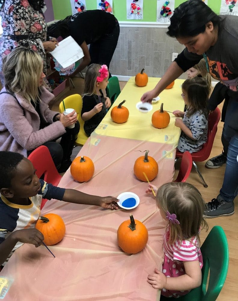 Adults and children painting pumpkins at a table