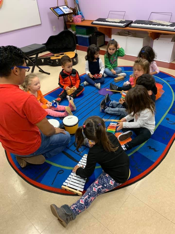 Adult and children sitting on a rug playing musical instruments