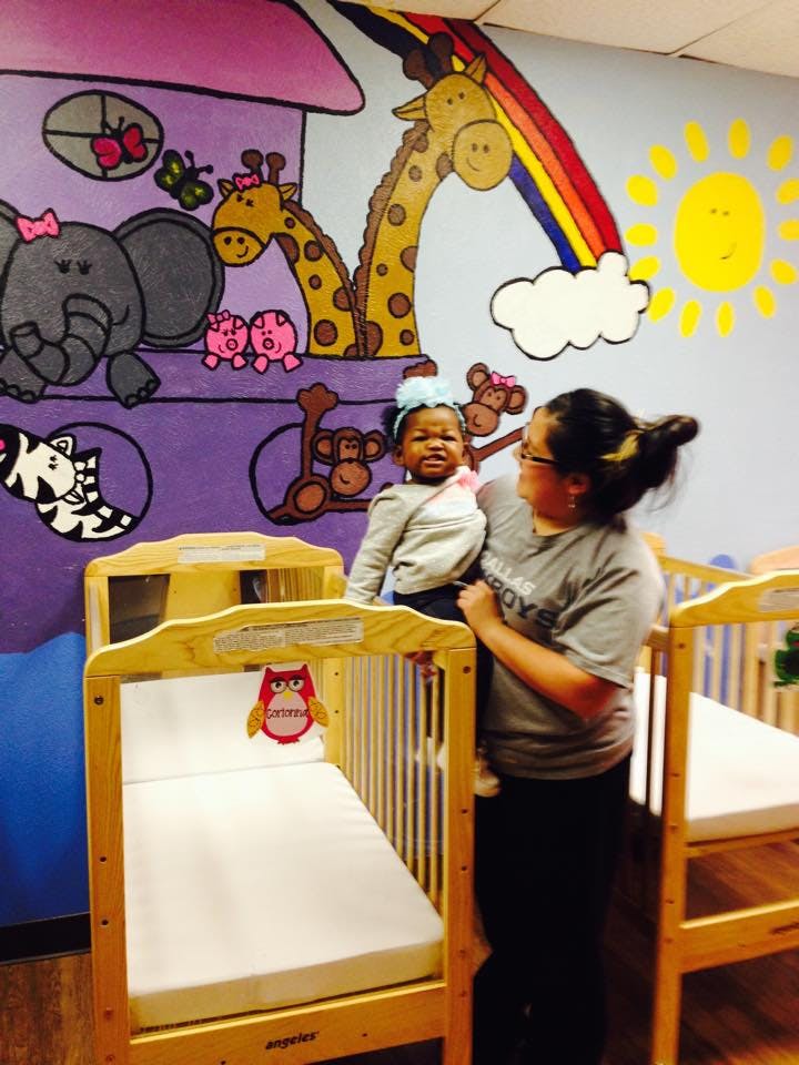 Person holding a child next to a crib in a room with animal murals