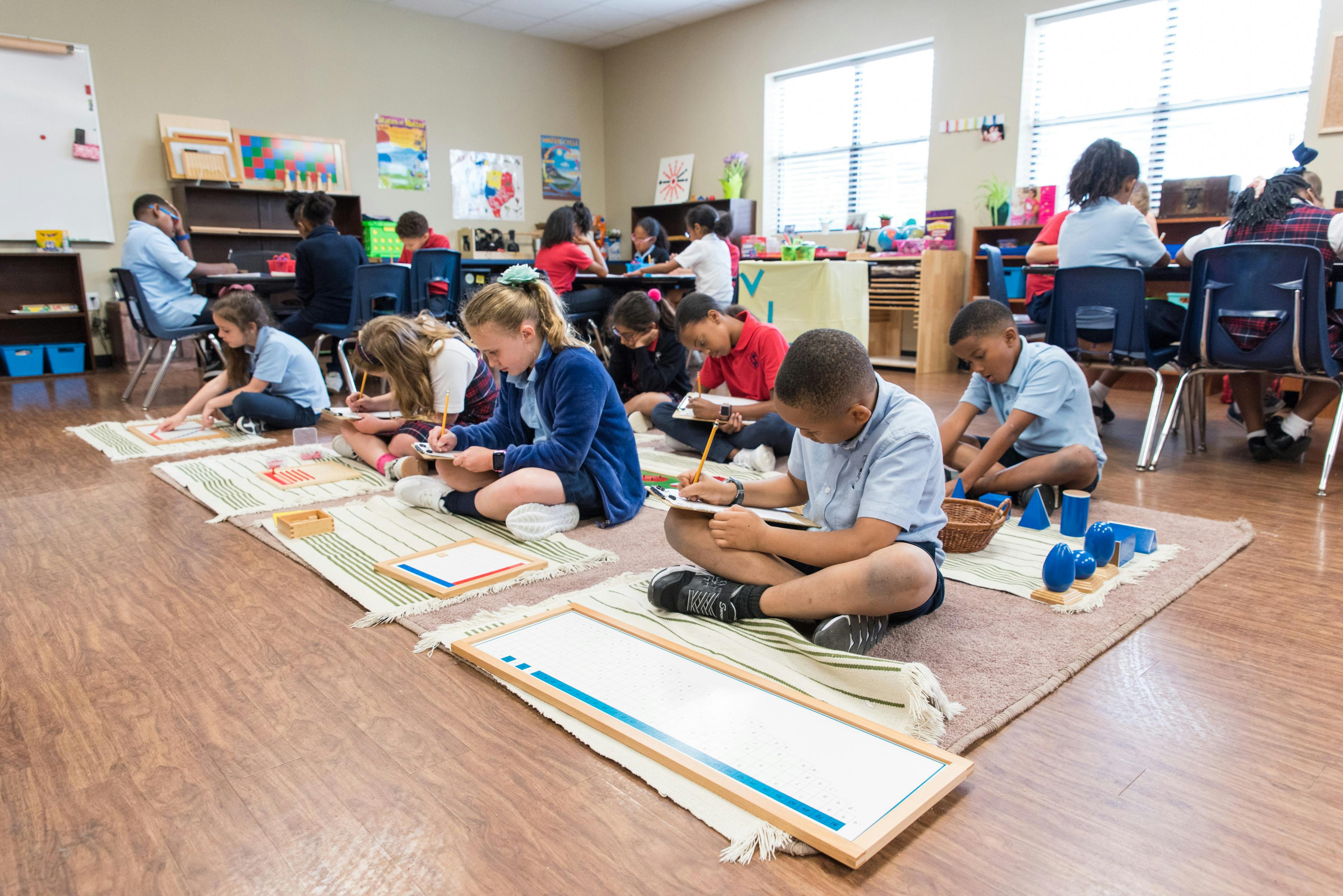 Children sitting on floor mats working on individual activities in a classroom