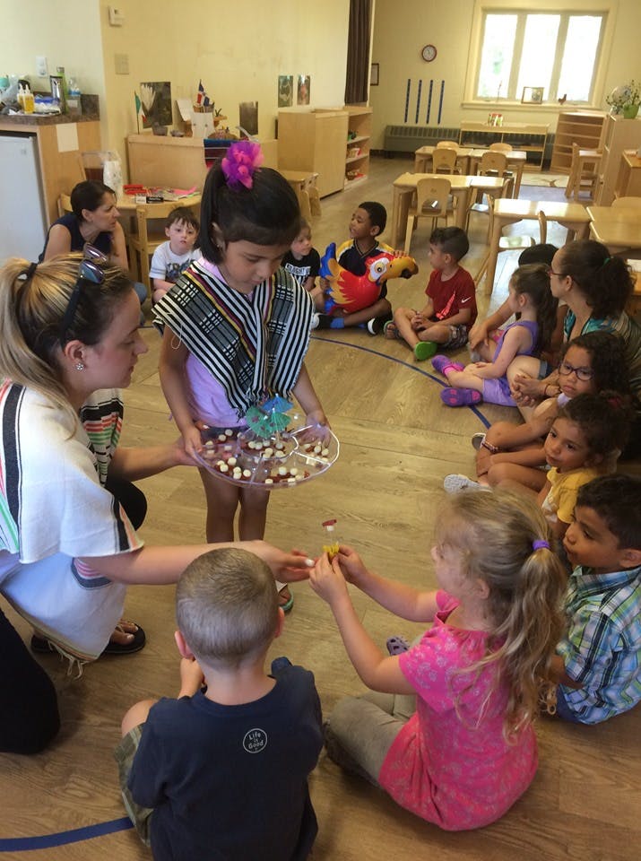 Adult and child helping another child distribute items from a tray to other children